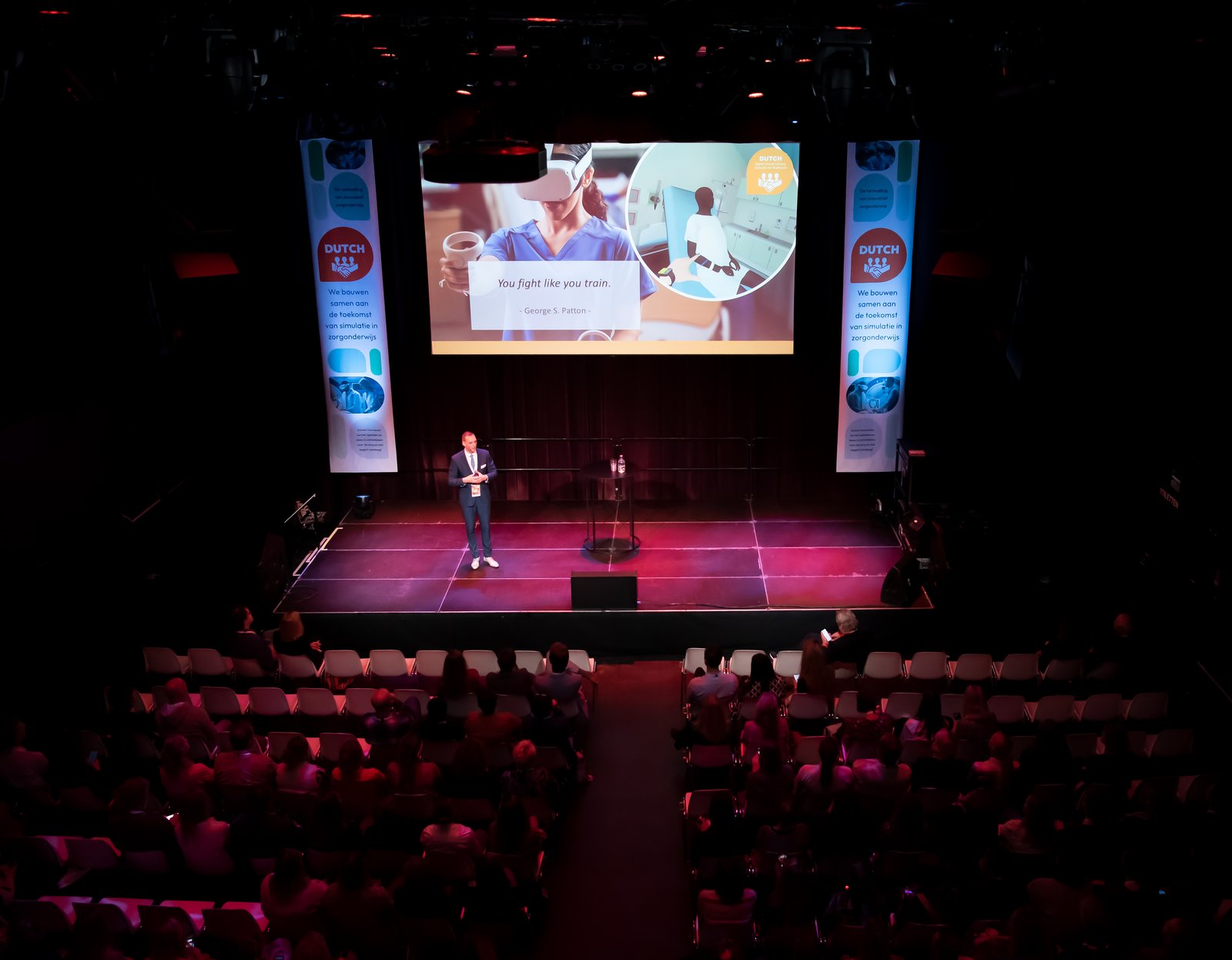 Leander op het podium voor een volle zaal tijdens een congres